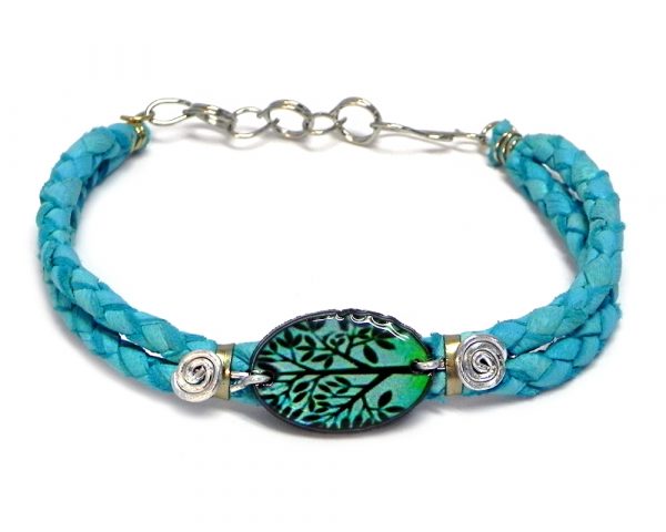 Handmade braided dyed leather bracelet with silver metal wire and oval-shaped acrylic New Age themed tree of life graphic design centerpiece in turquoise blue, mint green, and black color combination.