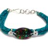 Handmade braided dyed leather bracelet with silver metal wire and oval-shaped acrylic New Age themed geometric hamsa hand graphic design centerpiece in teal green and multicolored color combination.