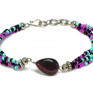 Handmade multicolored seed bead multi strand bracelet with teardrop-shaped cat’s eye glass bead centerpiece in dark purple, magenta purple, mint green, and black color combination.