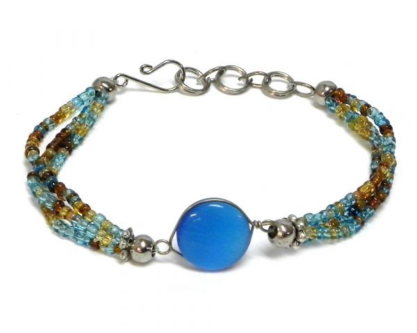 Handmade multicolored seed bead multi strand bracelet with round-shaped cat’s eye glass bead centerpiece in light blue, turquoise, gold, and brown color combination.