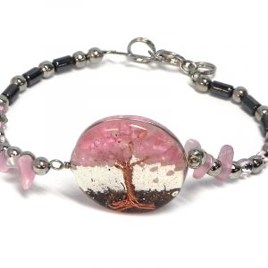 Handmade hematite, chip stone, and silver metal seed bead bracelet with round-shaped clear acrylic resin, copper wire, and crushed chip stone inlay tree of life centerpiece in pink color.