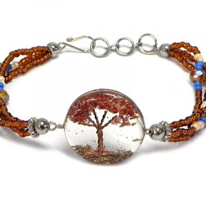 Handmade crystal bead and seed bead multi strand bracelet with round-shaped clear acrylic resin, copper wire, and crushed chip stone inlay tree of life centerpiece in orange brown goldstone, brown, blue, and beige color combination.