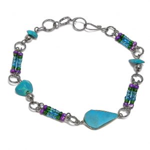 Handmade chip stone and multicolored seed bead silver metal chain bracelet with teardrop-cut turquoise howlite gemstone crystal cabochon centerpiece in purple, green, and turquoise blue color combination.