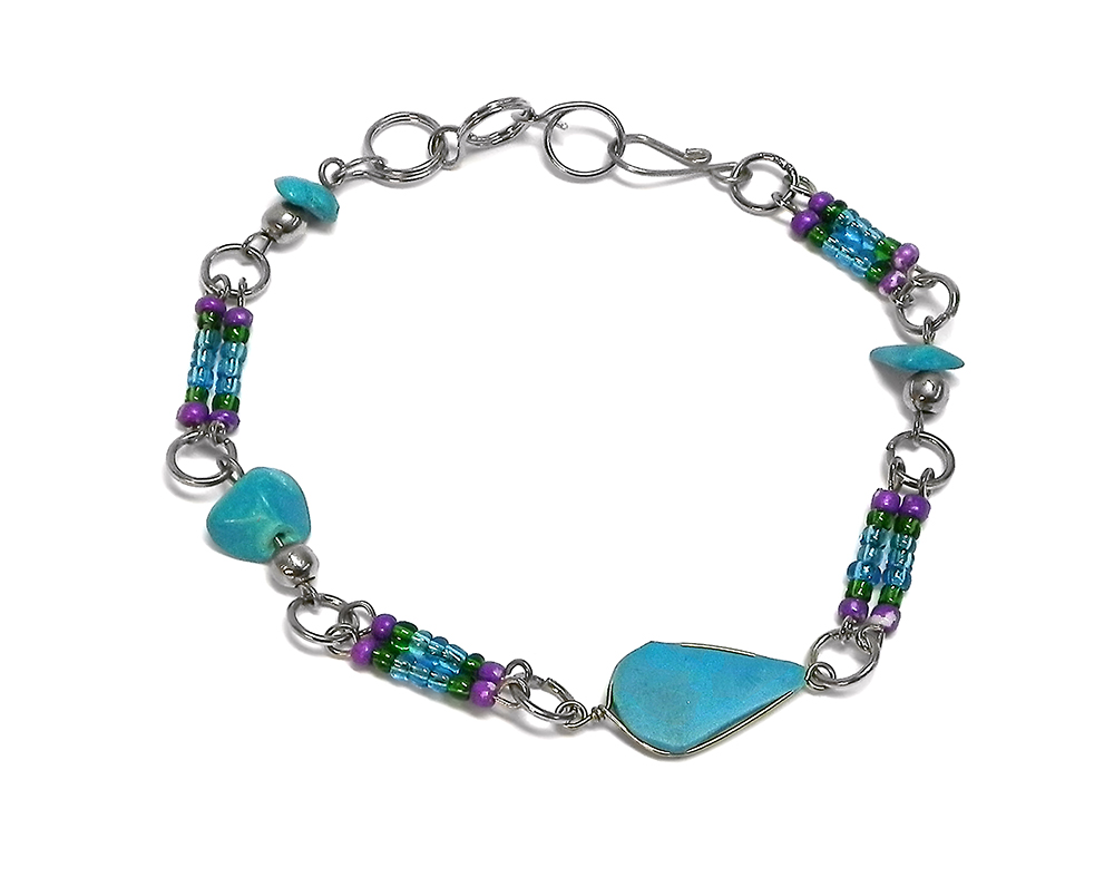 Handmade chip stone and multicolored seed bead silver metal chain bracelet with teardrop-cut turquoise howlite gemstone crystal cabochon centerpiece in purple, green, and turquoise blue color combination.
