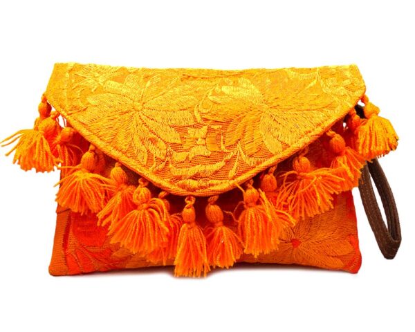 Handmade slim envelope purse bag with floral embroidered cotton material, pom pom fringe, magnetic snap closure, and a wristlet strap in orange color.