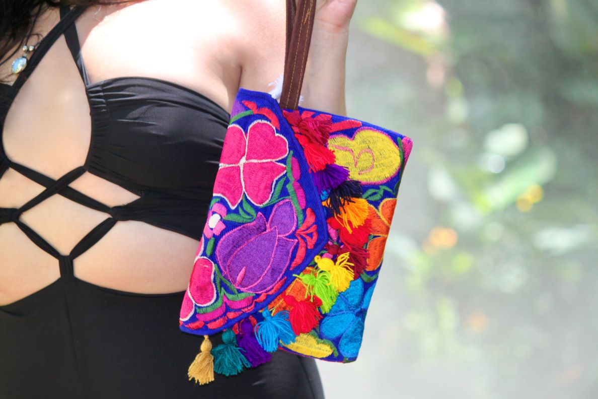 Handmade slim envelope purse bag with floral embroidered cotton material, pom pom fringe, magnetic snap closure, and a wristlet strap in blue and multicolored color combination.