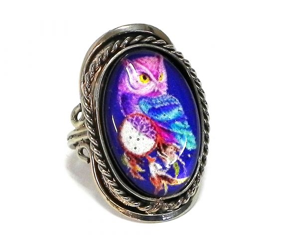 Handmade oval-shaped acrylic New Age themed dream catcher owl graphic design on alpaca silver metal ring with rope edge border in blue, purple, yellow, turquoise, brown, and white color combination.