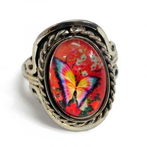 Handmade small oval-shaped acrylic vintage themed butterfly graphic design on alpaca silver metal ring with rope edge border in red-orange, orange, hot pink, dark green, and white color combination.