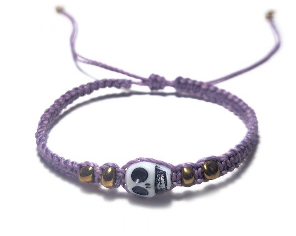 Handmade macramé braided string pull tie bracelet with gold colored seed beads and white skull shaped bead centerpiece in lavender purple color.