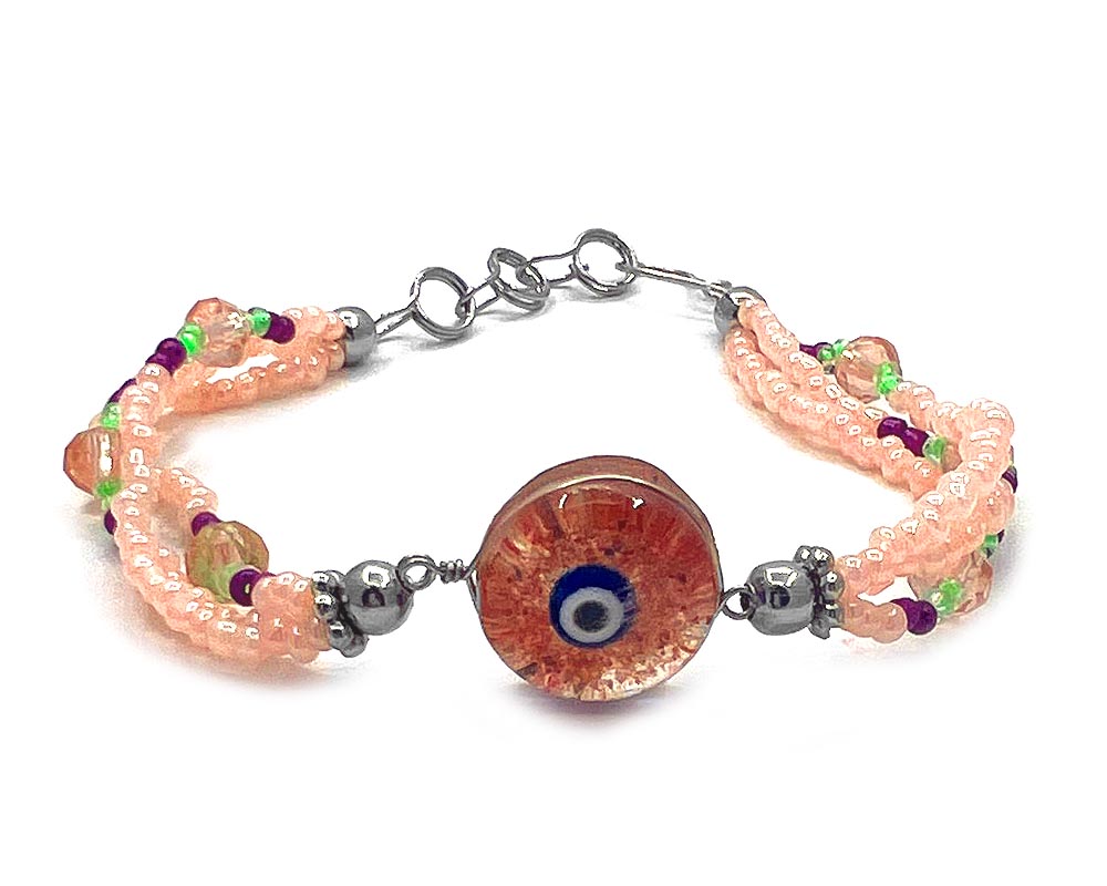 Handmade seed bead and crystal bead multi strand bracelet with round-shaped clear acrylic resin and crushed chip stone inlay evil eye centerpiece in orange, peach, blue, black, and white color combination.